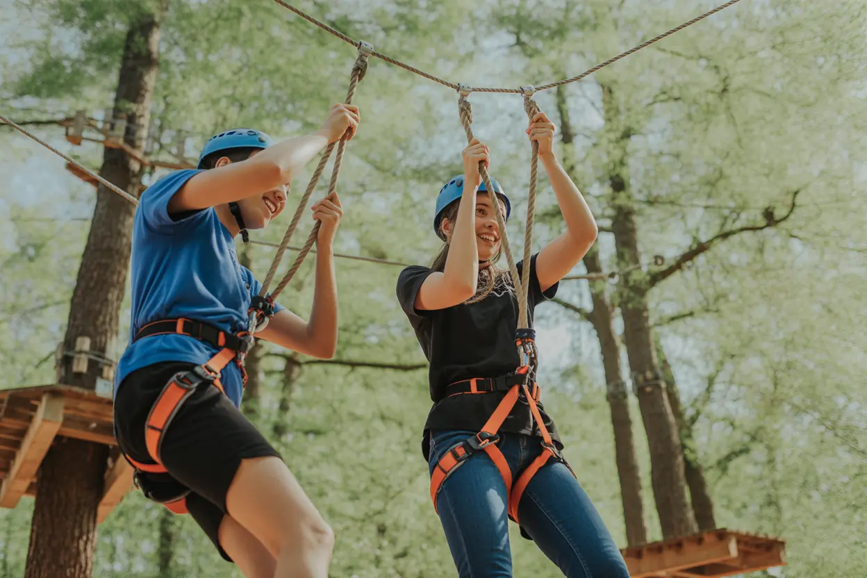 Two people working together on a low-ropes course, demonstrating teamwork and support during an adventure therapy activity.