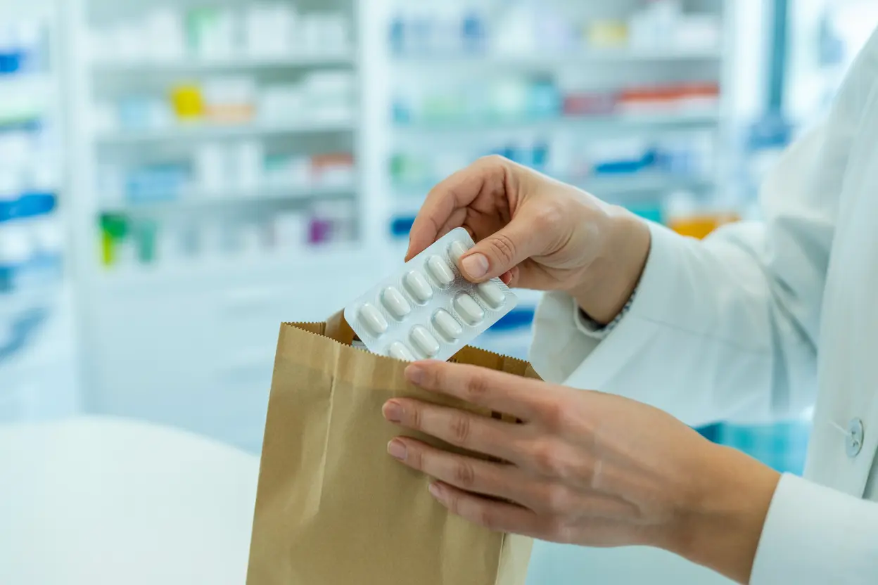 A pharmacist's hands carefully placing medication into a paper bag, representing professional and supportive care.