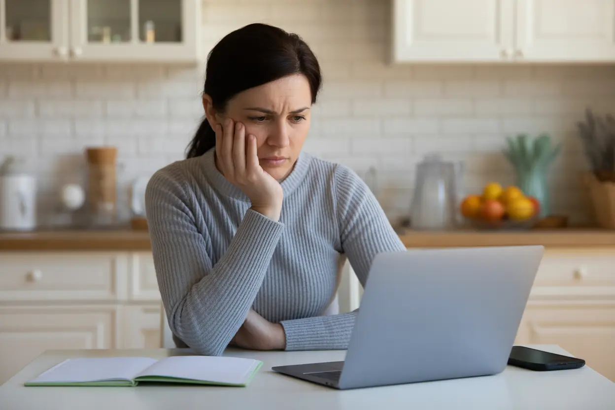 A concerned parent researches child rehab options on a laptop at their kitchen table.