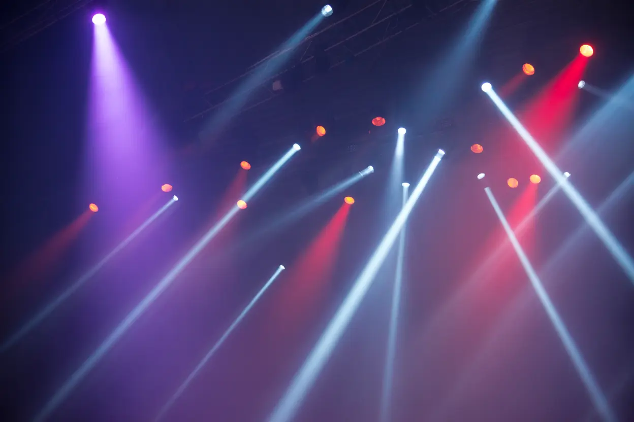 An abstract, artistic photo of colorful concert lights shining through a hazy atmosphere, creating a vibrant but distant mood.