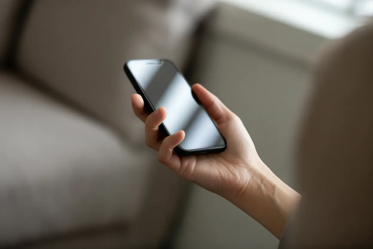 A person's hand holding a smartphone, ready to make a call for help.
