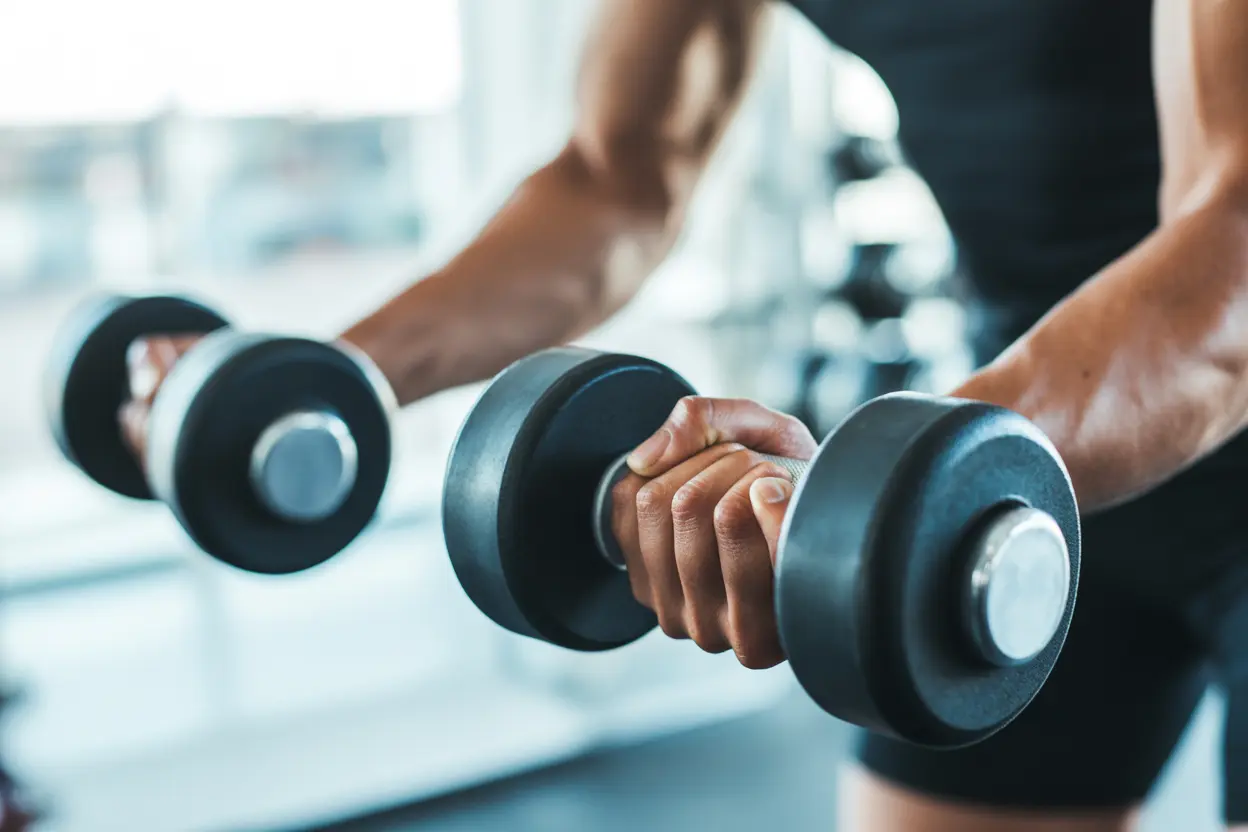 Close-up of hands gripping a dumbbell during a controlled bicep curl exercise in a gym.