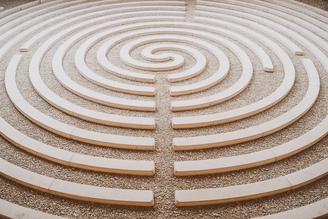 A top-down view of a stone labyrinth path set on fine gravel, showing a single, clear path to the center.