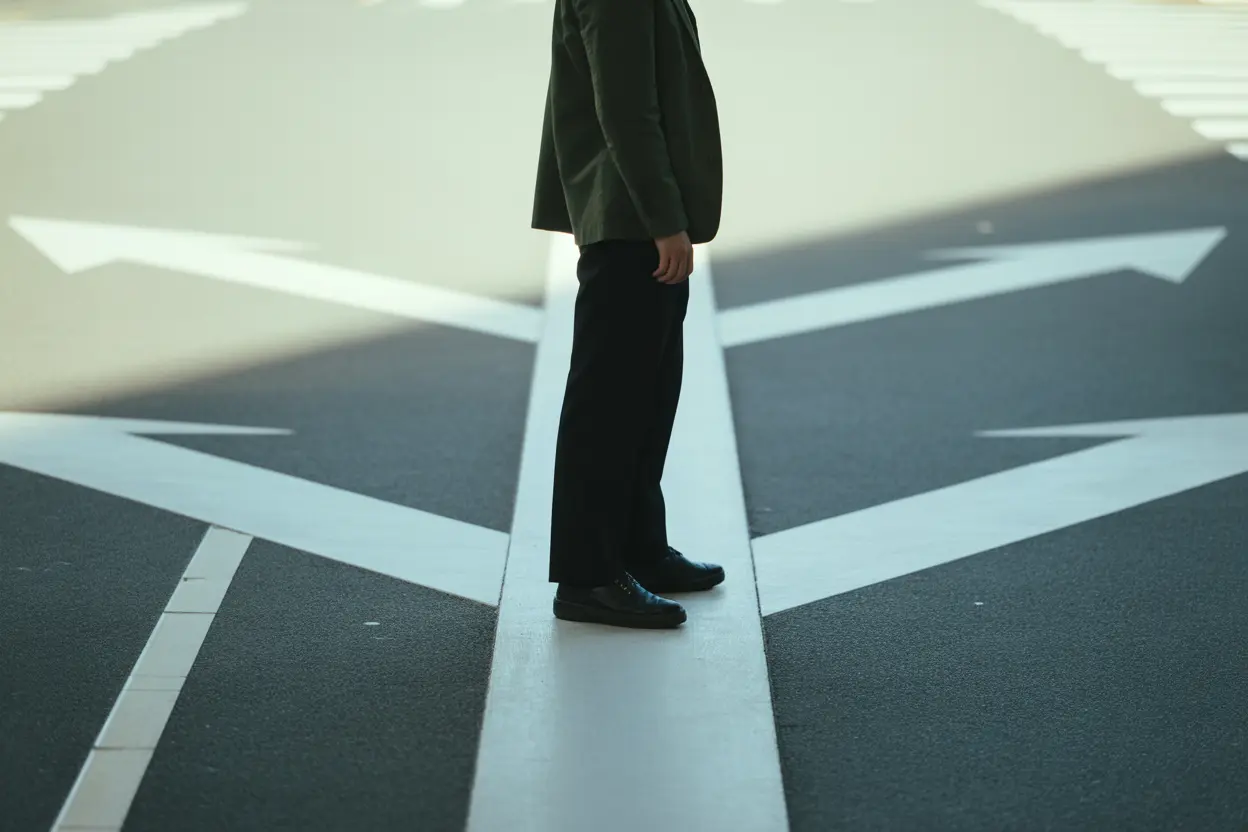 A person stands at a crossroads, looking thoughtfully down one path in a minimalist urban setting.