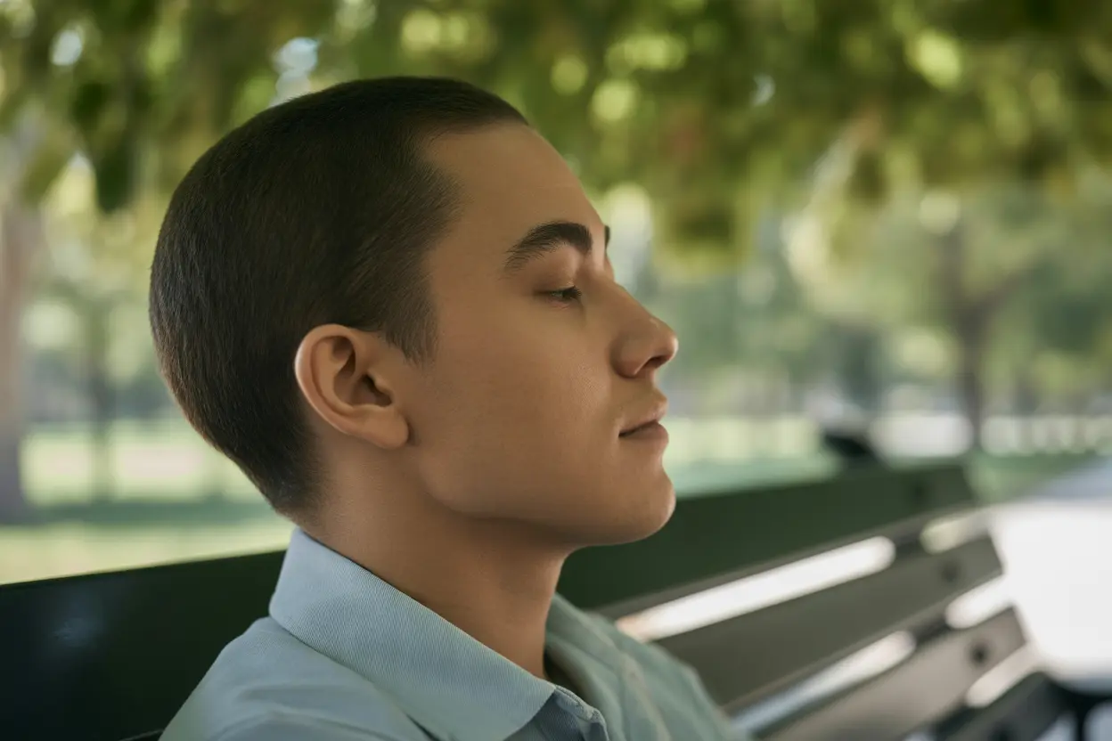 A person sits peacefully on a park bench with their eyes closed, practicing mindfulness in the sunlight.