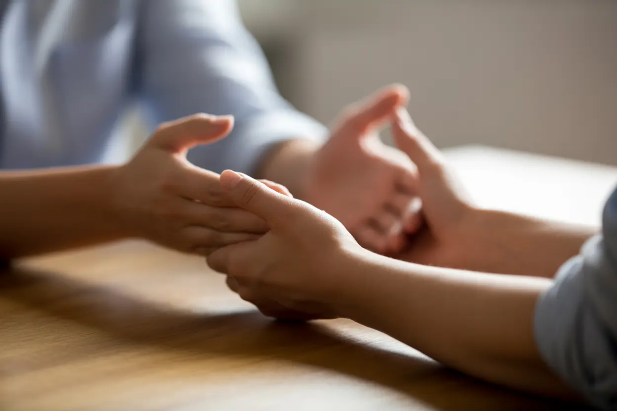 Two hands on a wooden table, one offering a supportive gesture, representing the therapeutic alliance in MBT.