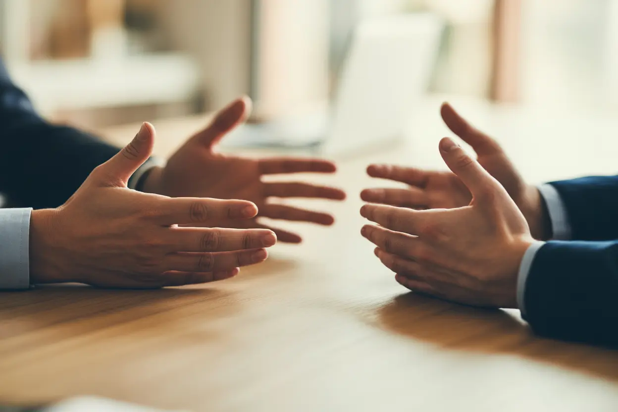 Two people's hands on a wooden table, one pair gesturing during a therapy session.